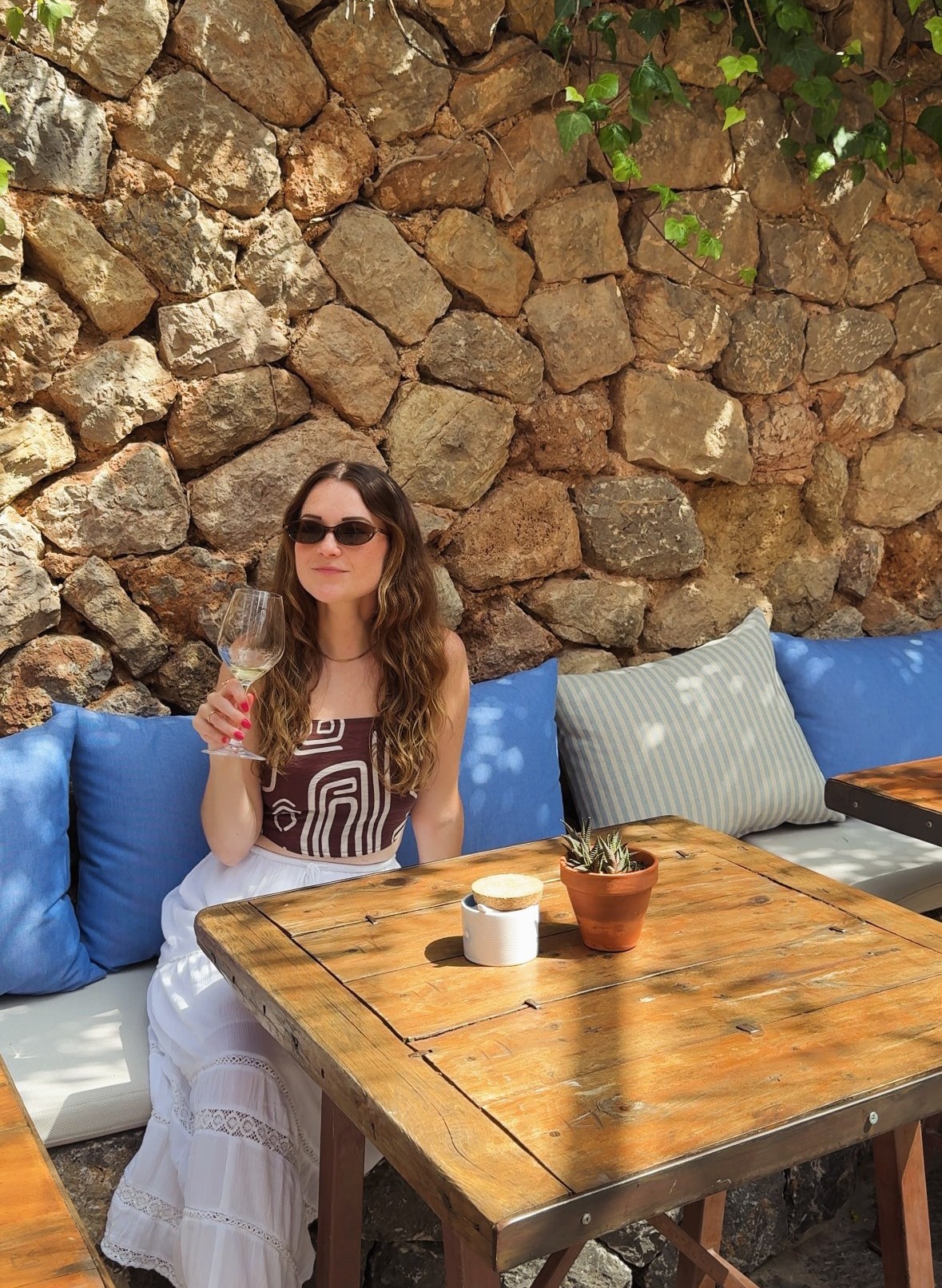 Mel at a table by a stone wall